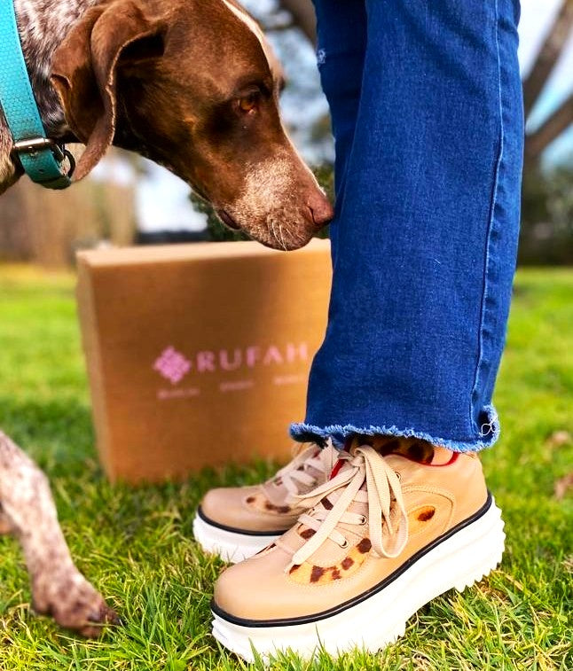 Zapatillas de cuero color beige siendo usadas por una modelo. En la imagen hay un perro. Vista de lado