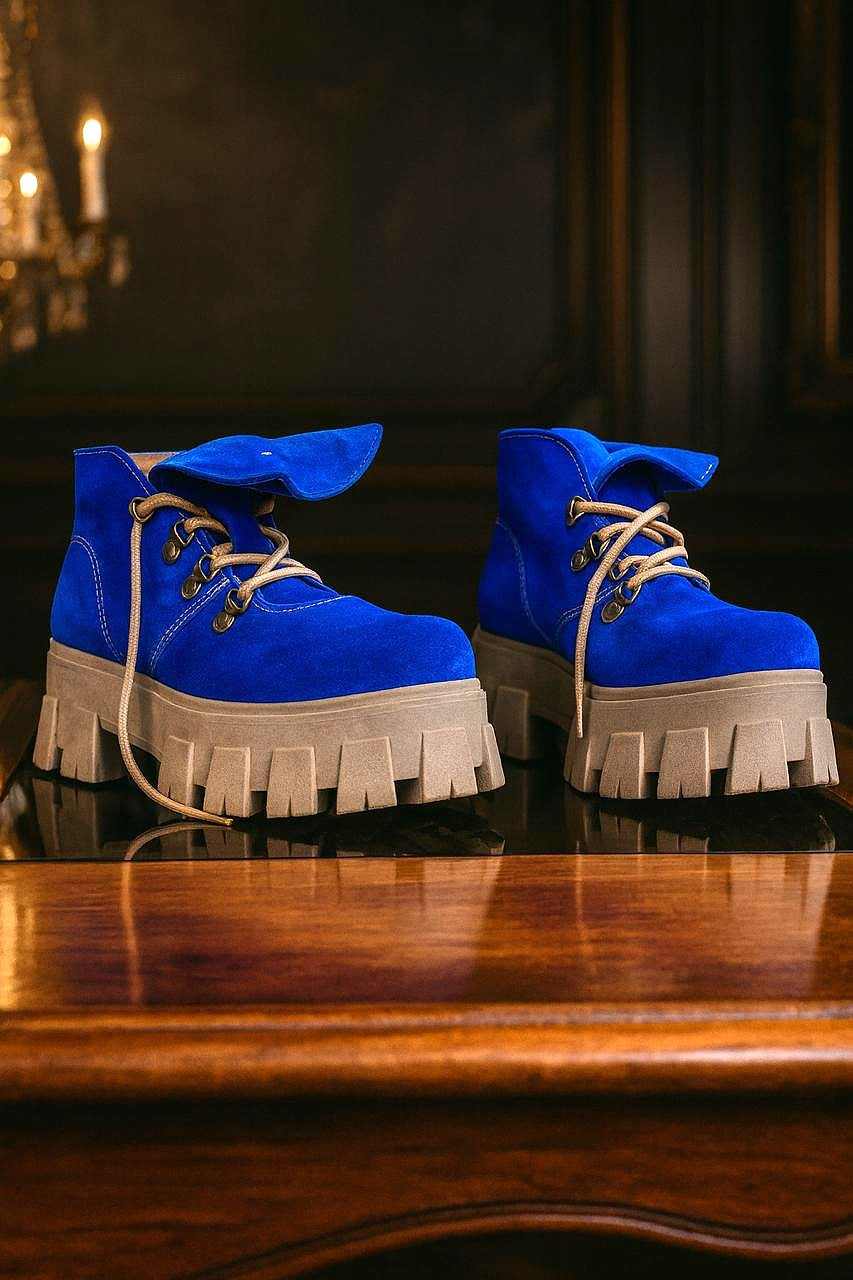 Par de botines de cuero color azul para mujer, con cordones y suela de plataforma dentada, visto de lado sobre superficie de madera