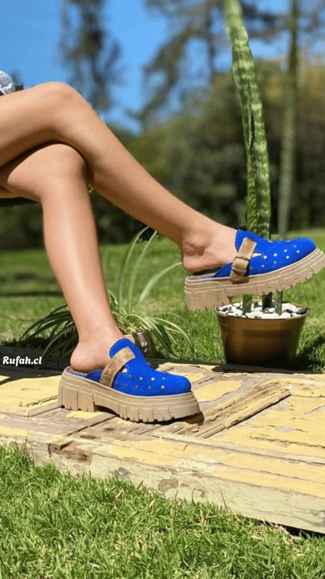 Mujer usando sueco de cuero color azul para mujer, con tachas metálicas decorativas, correa con hebilla y suela de plataforma al aire libre. Vista lateral