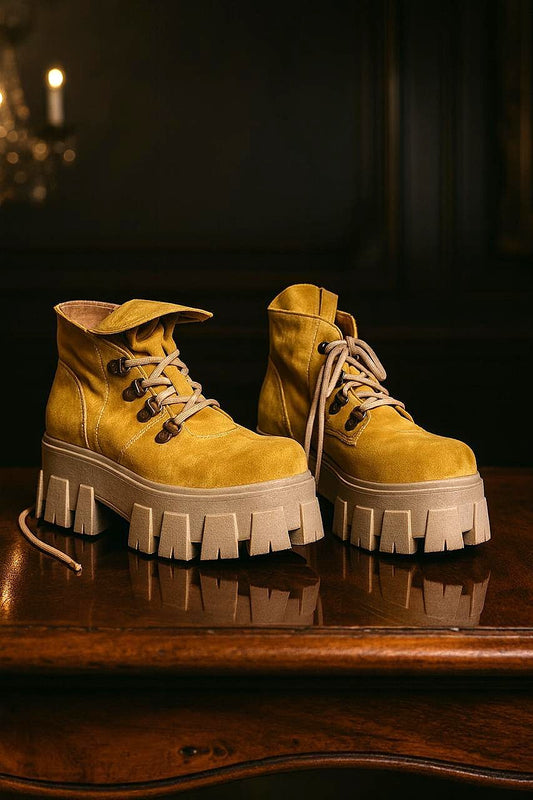 Par de botines de cuero color amarillo para mujer, con cordones y suela de plataforma dentada, visto de lado sobre superficie de madera