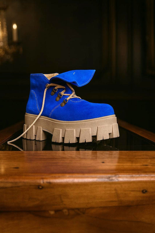 Botín de cuero color azul para mujer, con cordones y suela de plataforma dentada, visto de lado sobre superficie de madera