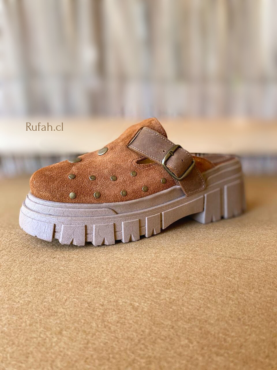 Sueco de cuero color café para mujer, con tachas metálicas decorativas, correa con hebilla y suela de plataforma. Vista lateral