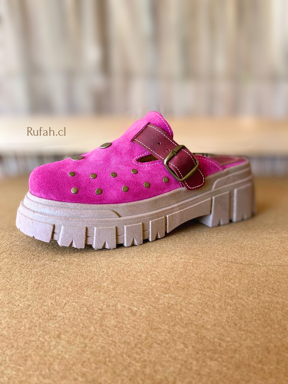 Sueco de cuero color fucsia para mujer, con tachas metálicas decorativas, correa con hebilla y suela de plataforma. Vista lateral