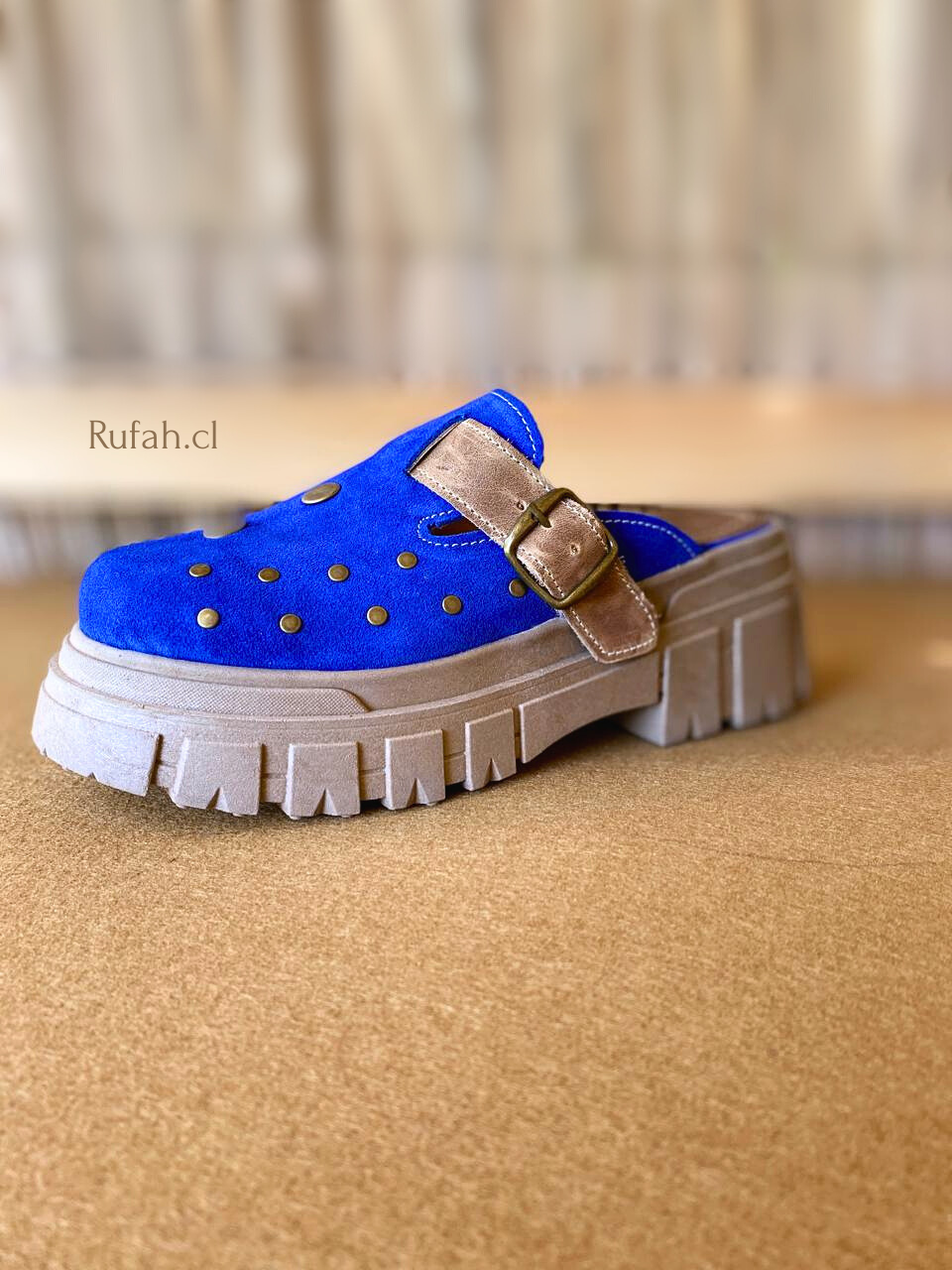 Sueco de cuero color azul para mujer, con tachas metálicas decorativas, correa con hebilla y suela de plataforma. Vista lateral