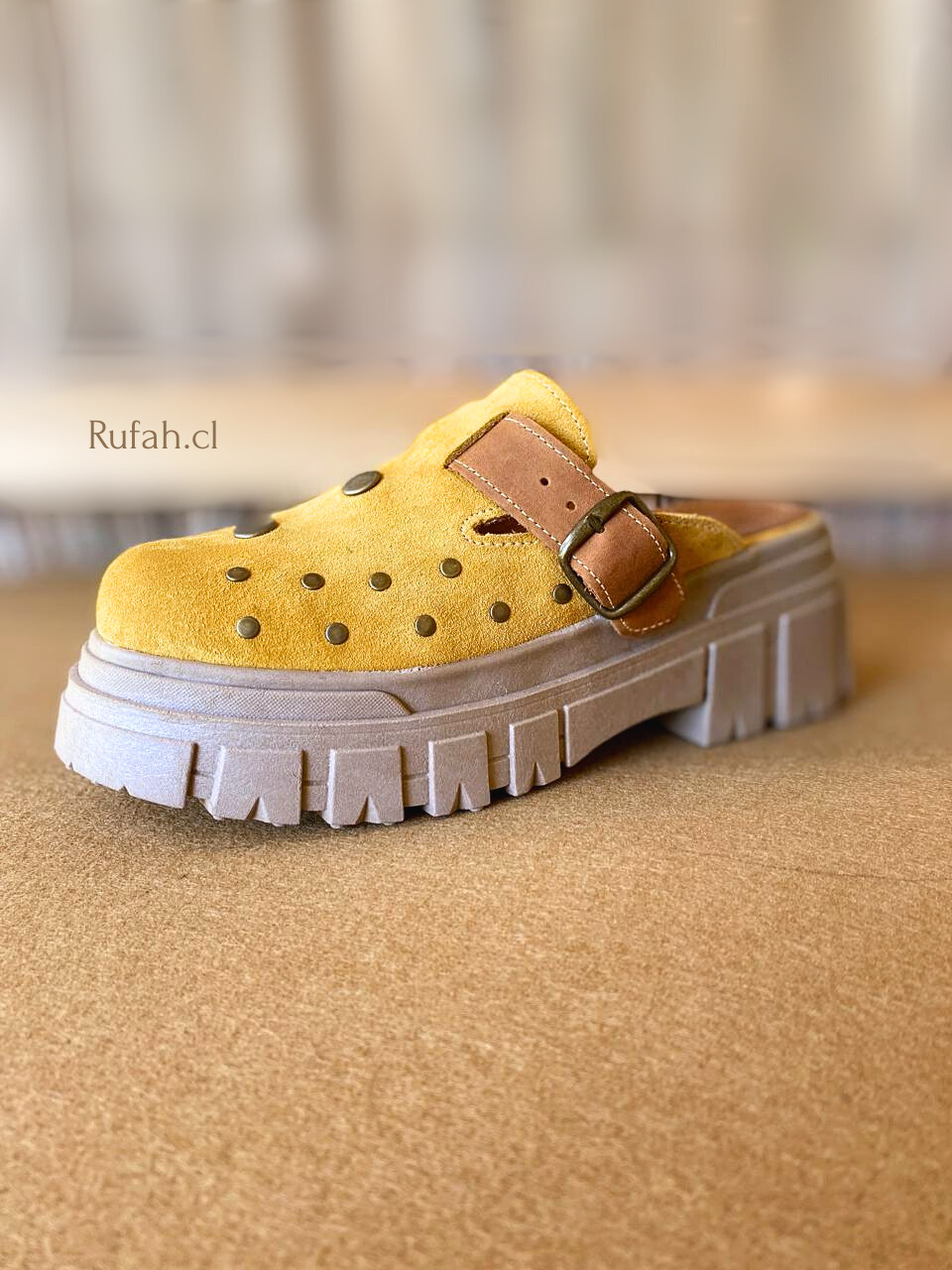 Sueco de cuero color amarillo para mujer, con tachas metálicas decorativas, correa con hebilla y suela de plataforma.