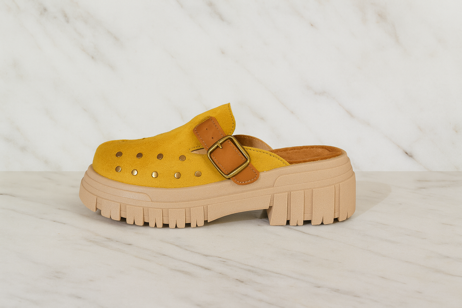 Sueco de cuero amarillo Rufah con suela chunky beige sobre fondo de mármol, destacado del mes.