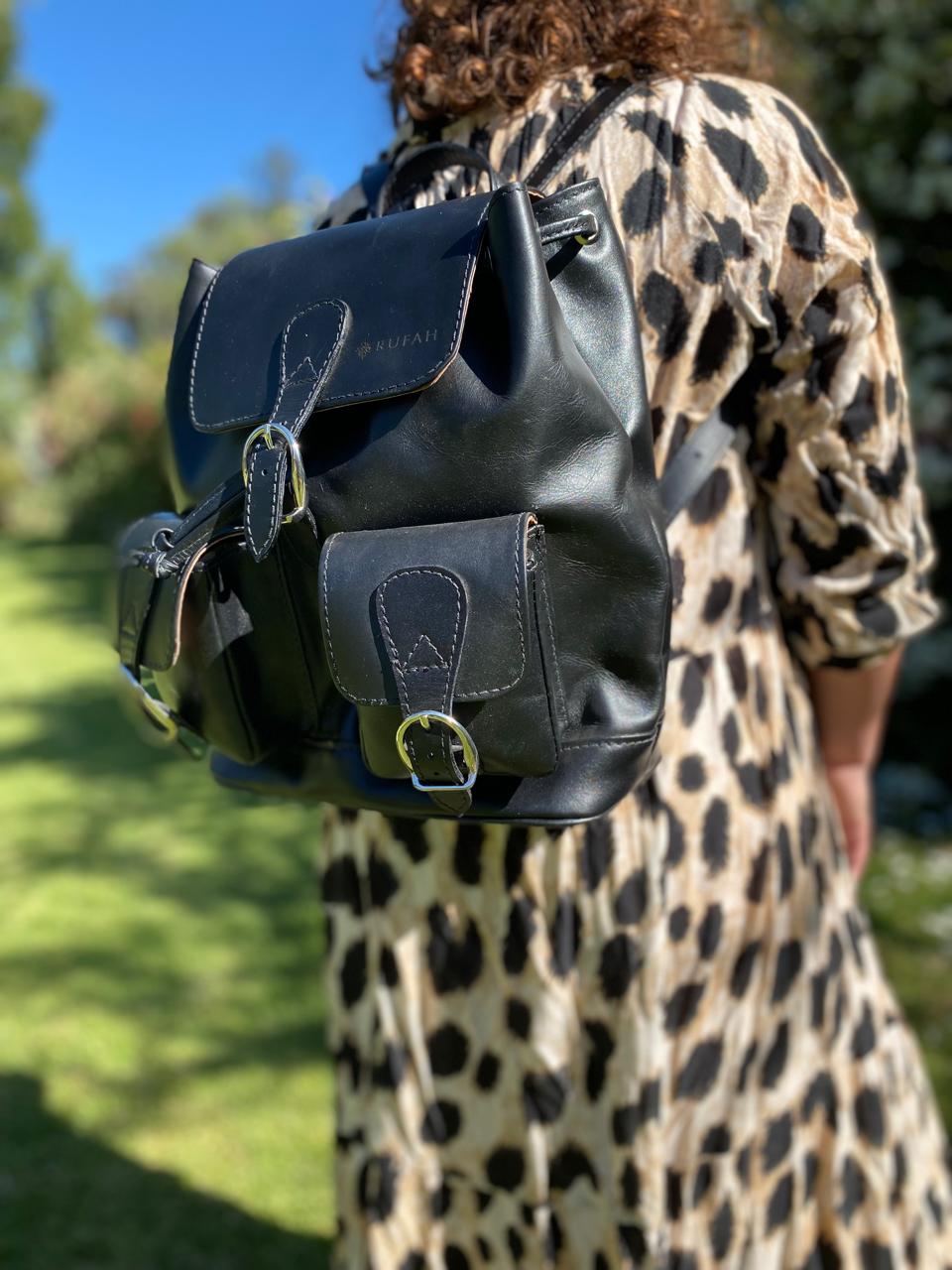 Mochila de cuero negro artesanal Rufah con bolsillos frontales y hebillas metálicas, llevada por una mujer en un entorno natural con vista frontal