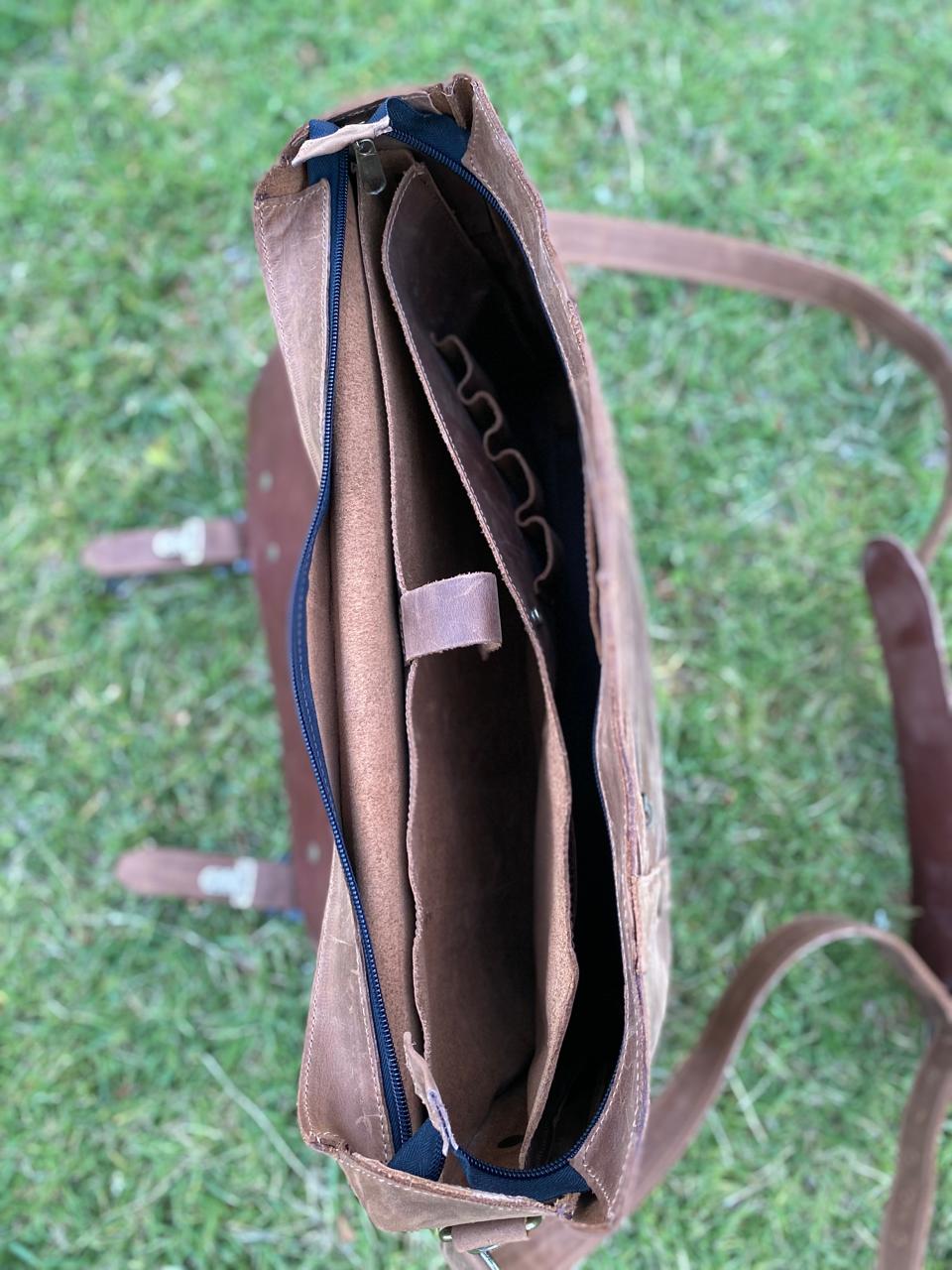 Maletín de cuero natural, con correa, hebillas metálicas, fotografiado al aire libre. Vista desde arriba