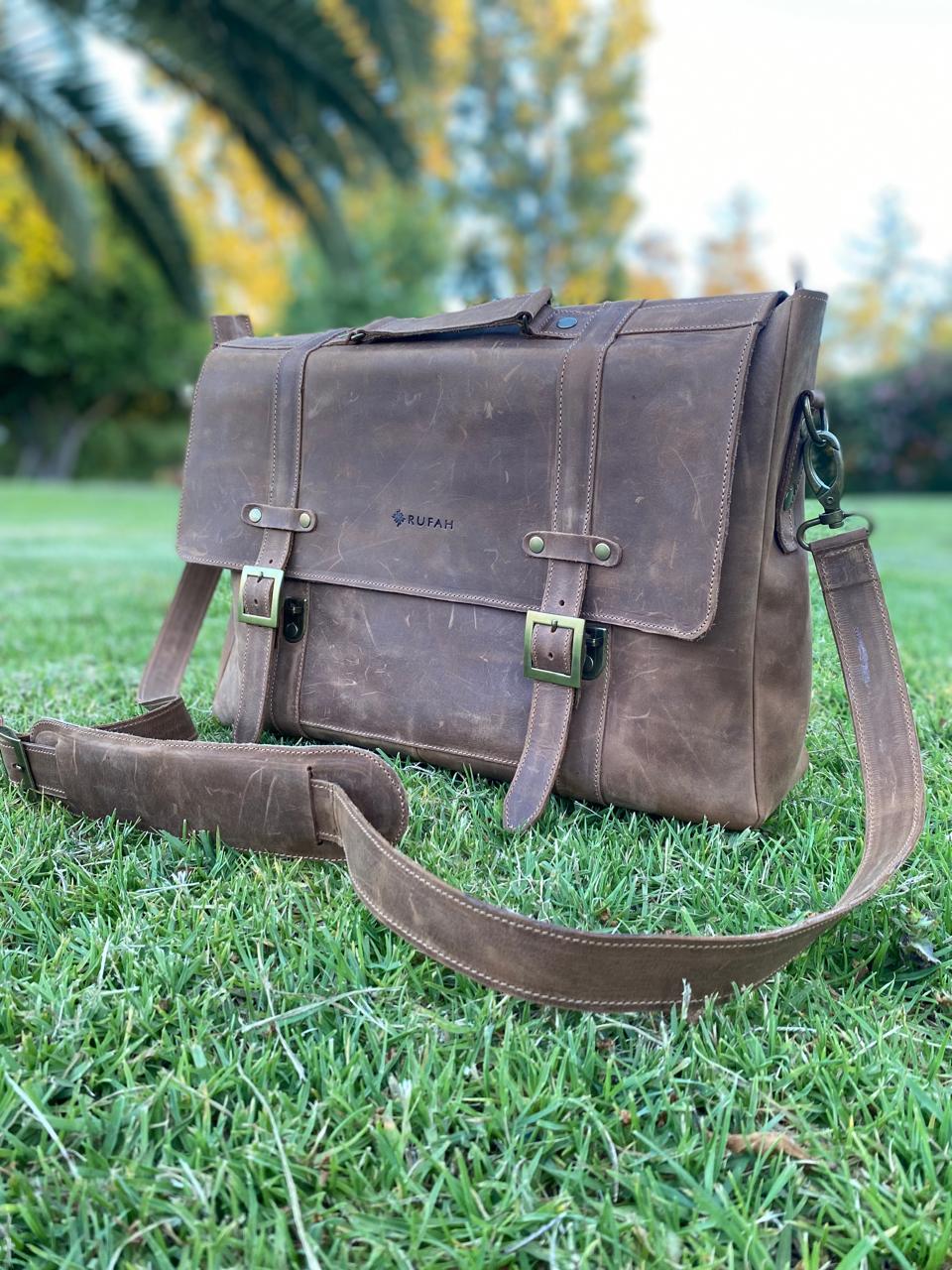 Maletín de cuero natural, con correa, hebillas metálicas, fotografiado al aire libre. Vista lateral