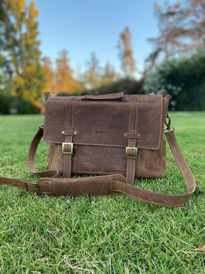 Maletín de cuero natural, con correa, hebillas metálicas, fotografiado al aire libre. Vista frontal